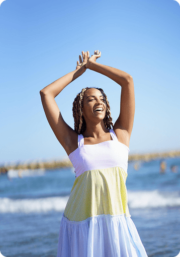 Woman smiling with arms raised by the beach, representing positive therapy results and emotional growth in a child